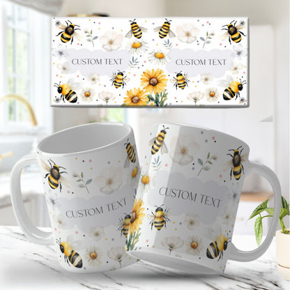 Two white floral mug desgins with bee and flower design on a matching box, set against a bright indoor background.